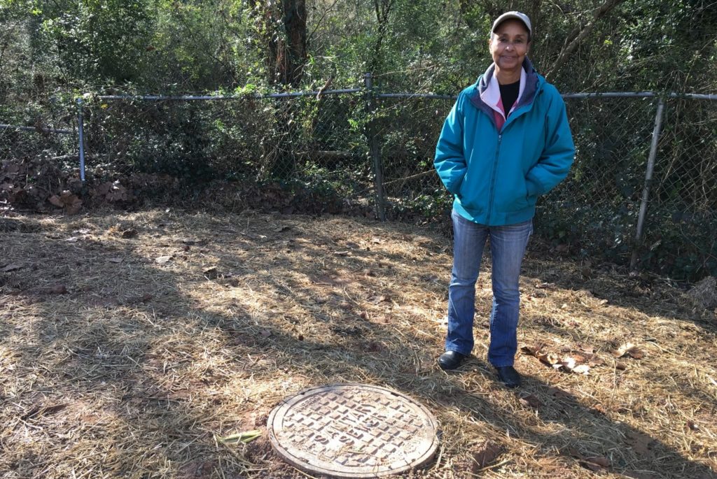 Jackie Echols, president of the South River Watershed Alliance, stands next to a manhole in another DeKalb County backyard. There have been a number of large sewage spills at this location, and last year the county bought the house, in order to do work on the sewer problems there. (Molly Samuel/WABE)