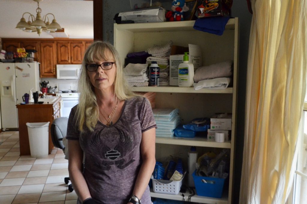 Lisa Archibald stands beside a shelf of medical supplies in what used to be her living room. She converted the space to care for her brother, John-David Mixon. (Sam Whitehead/WABE)