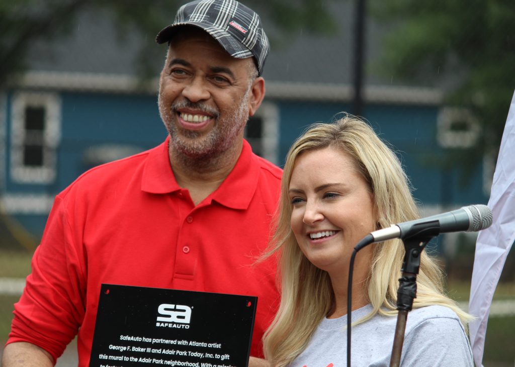 J. Lawrence Miller, president of the neighborhood group Adair Park Today receives a plaque from Amber Yeray of SafeAuto. The insurance company commissioned the new mural in Adair Park. (Emil Moffatt/WABE)