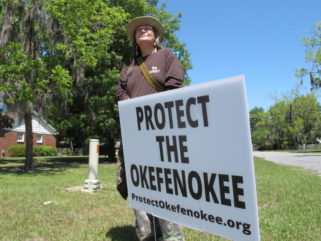 Jane Winkler stands with a sign that says "Protect The Okefenokee" outside a church where Gov. Brian Kemp met with local Chamber of Commerce members in Folkston on April 22. Winkler and others are fighting a mining company's plan to dig for minerals about 3 miles from the edge of the Okefenokee National Wildlife Refuge. Twin Pines Minerals says it can mine the area without harming the swamp. (Russ Bynum/Associated Press file)