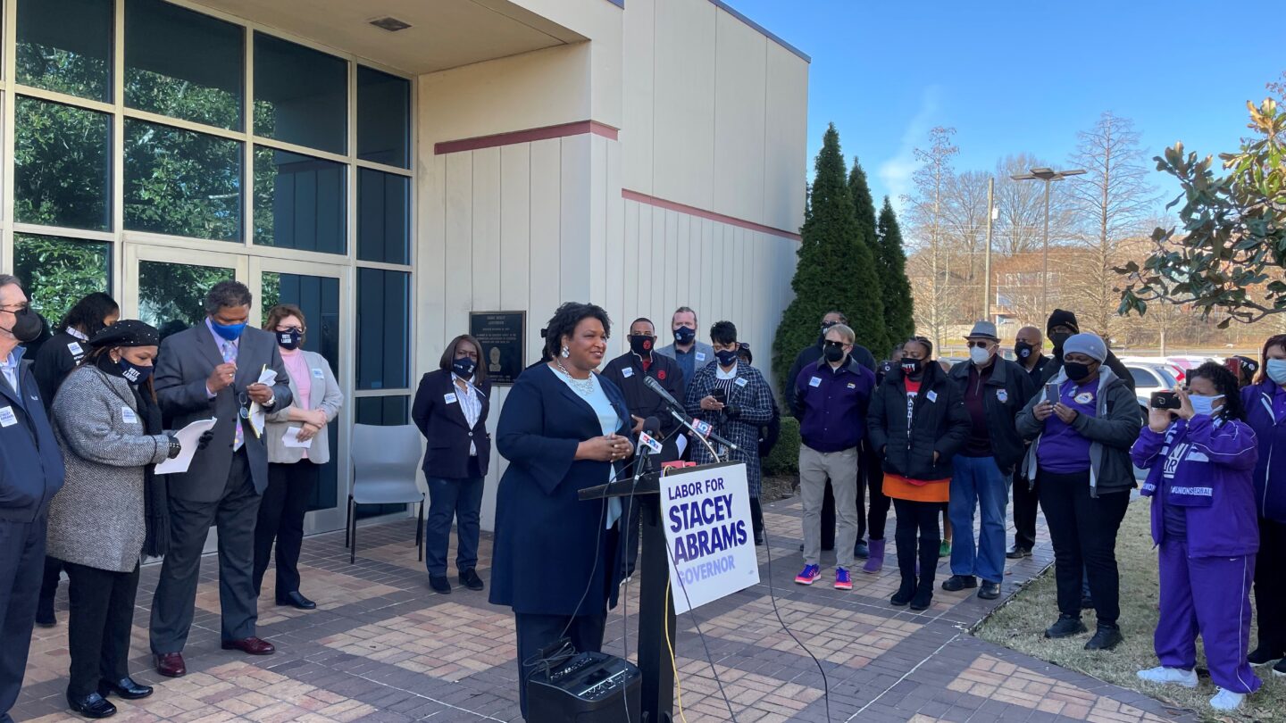 Democrat Stacey Abrams speaks from a lectern in front of an IBEW office in Atlanta.
