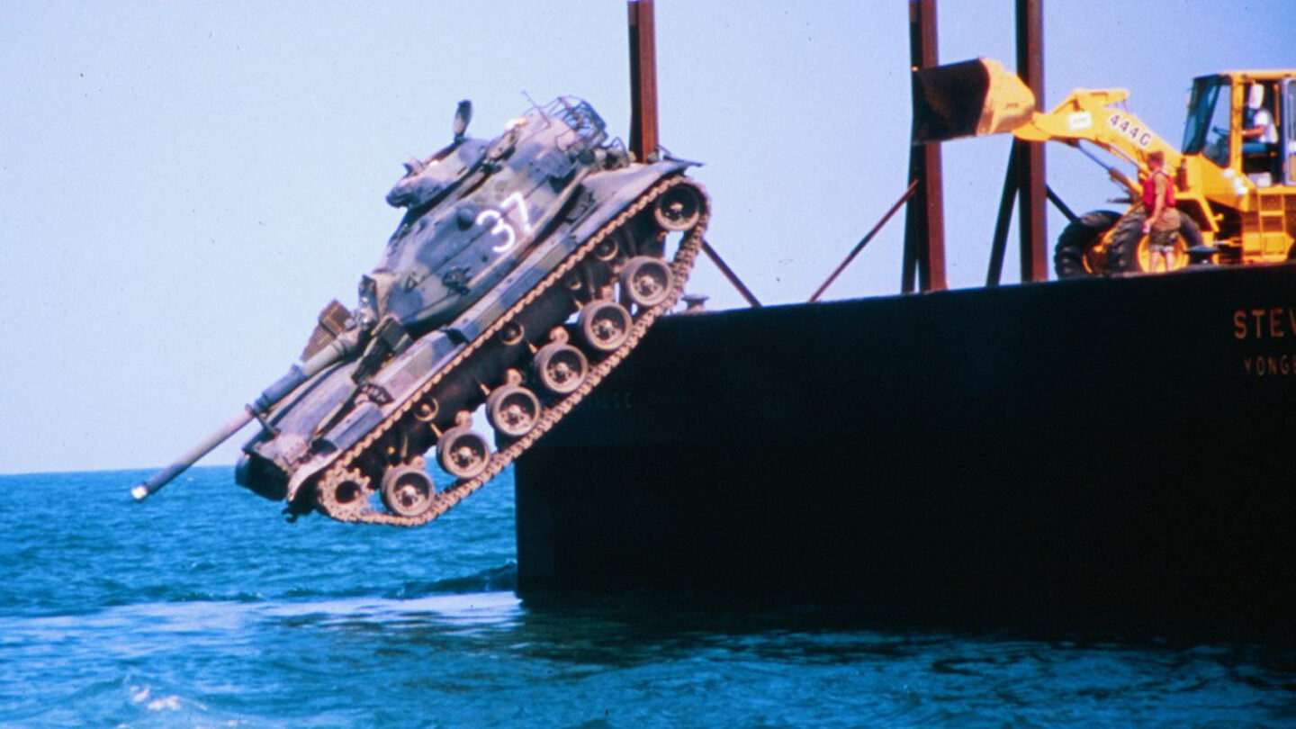 A battle tank is shoved off a barge into the ocean