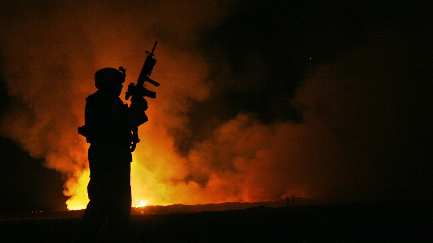 U.S. Marine Corps Sgt. Robert B. Brown, with Combat Camera Unit, Regimental Combat Team 6, watches over the civilian firefighters at the burn pit as smoke and flames rise into the night sky behind him in Camp Fallujah, Iraq. U.S. Marine Corps photo by Cpl. Samuel D. Corum. June 1, 2007 Flickr/Cpl. Samuel D. Corum.