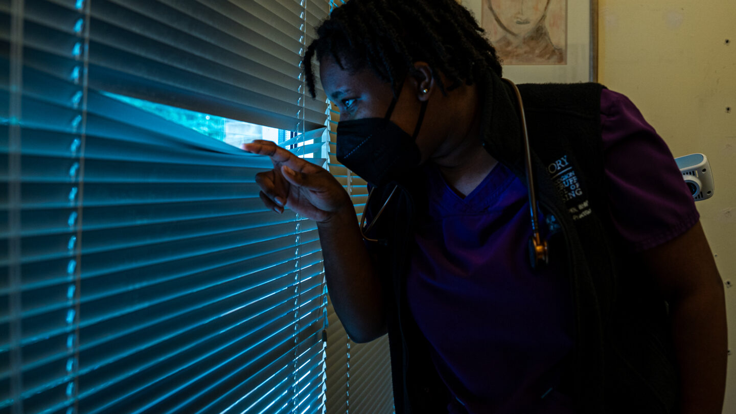 Aneisha Jacobs, a Nurse Practitioner and Nursing Supervisor at Feminist Women’s Health Center in Atlanta, peeks through the blinds to check on anti-abortion protesters on the street outside. The clinic provides abortion services and is a regular target of anti-abortion protesters. (Matt Pearson/WABE)