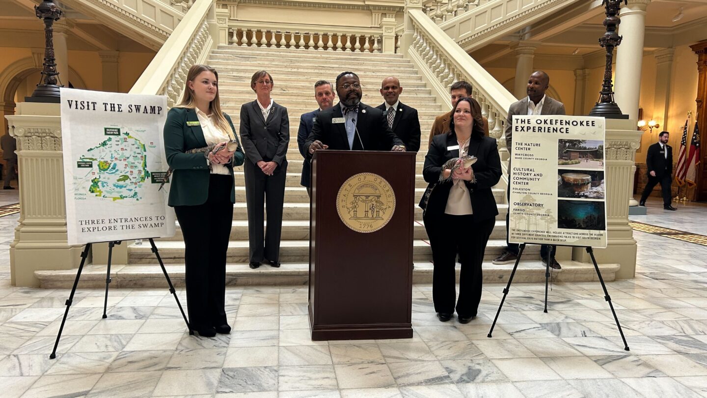 a group of people, two of them holding small alligators, make an announcement at a podium on the Georgia state capitol steps