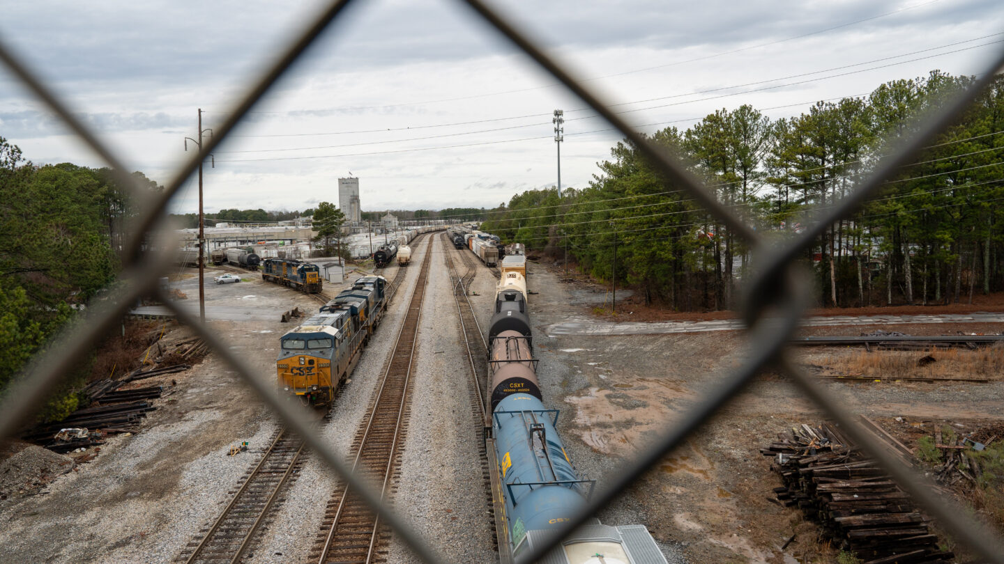 A freight train yard viewed through a chain link fence.