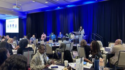 A group of people are on stage in a large conference room while there is an audience watching.
