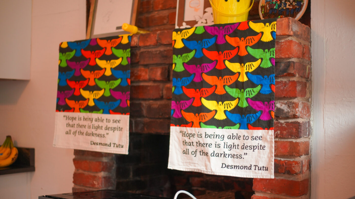 Two banners hanging from the fireplace mantle with black backgrounds and rainbow colored birds with a quote from Desmond Tutu that says Hope is being able to see that there is light despite all of the darkness