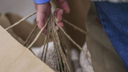 A closeup on a hand holding multiple brown paper shopping bags.