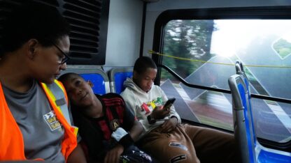 Elias Washington, right, plays on his phone along with his mother Sechita McNair, left, and adopted brother, Derrick McNair-White, center, as they ride the bus to Atlanta on June 11, 2025.