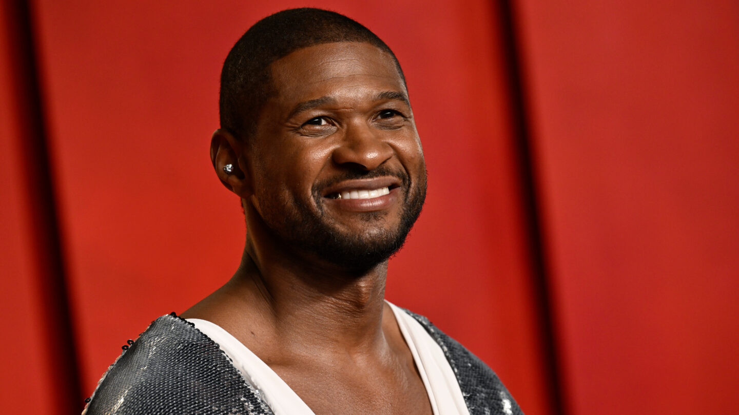 Usher smiles on a red carpet against a red background