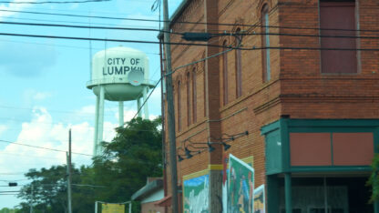 A water tower with black lettering that says City of Lumpkin, next to a brick building in Lumpkin, Georgia.
