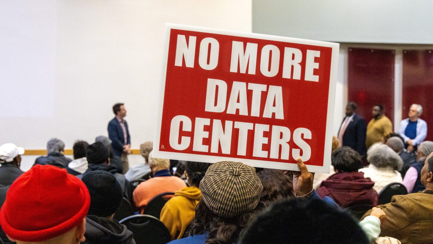 Someone holds up a red sign with white letters spelling out No More Data Centers