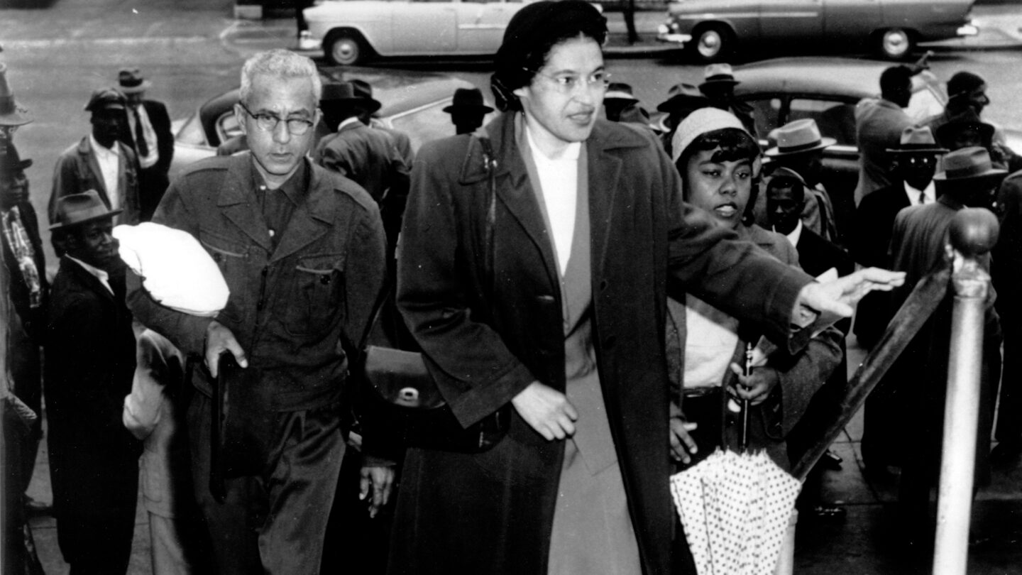 A black and white photo of Rosa Parks in 1956 walking up stairs in front of others.