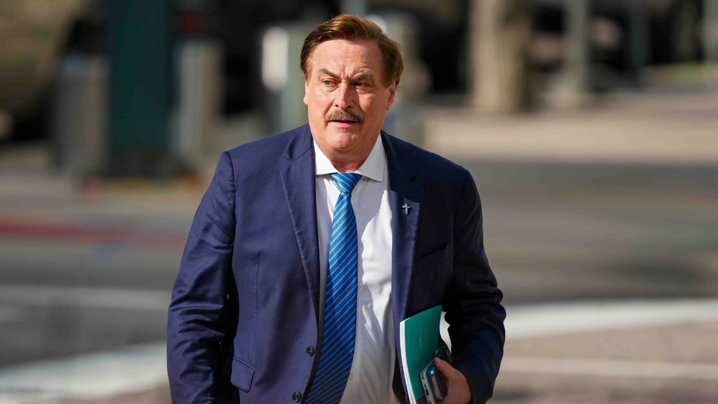 A man in a suit walks outside holding a folder