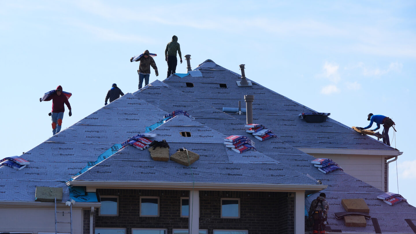 Workers on top of the roof of a house on a sunny day