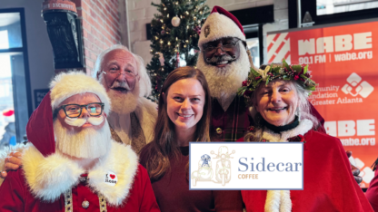 A group of Santa Clauses and a Mrs. Claus gather around a cafe owner for a photo