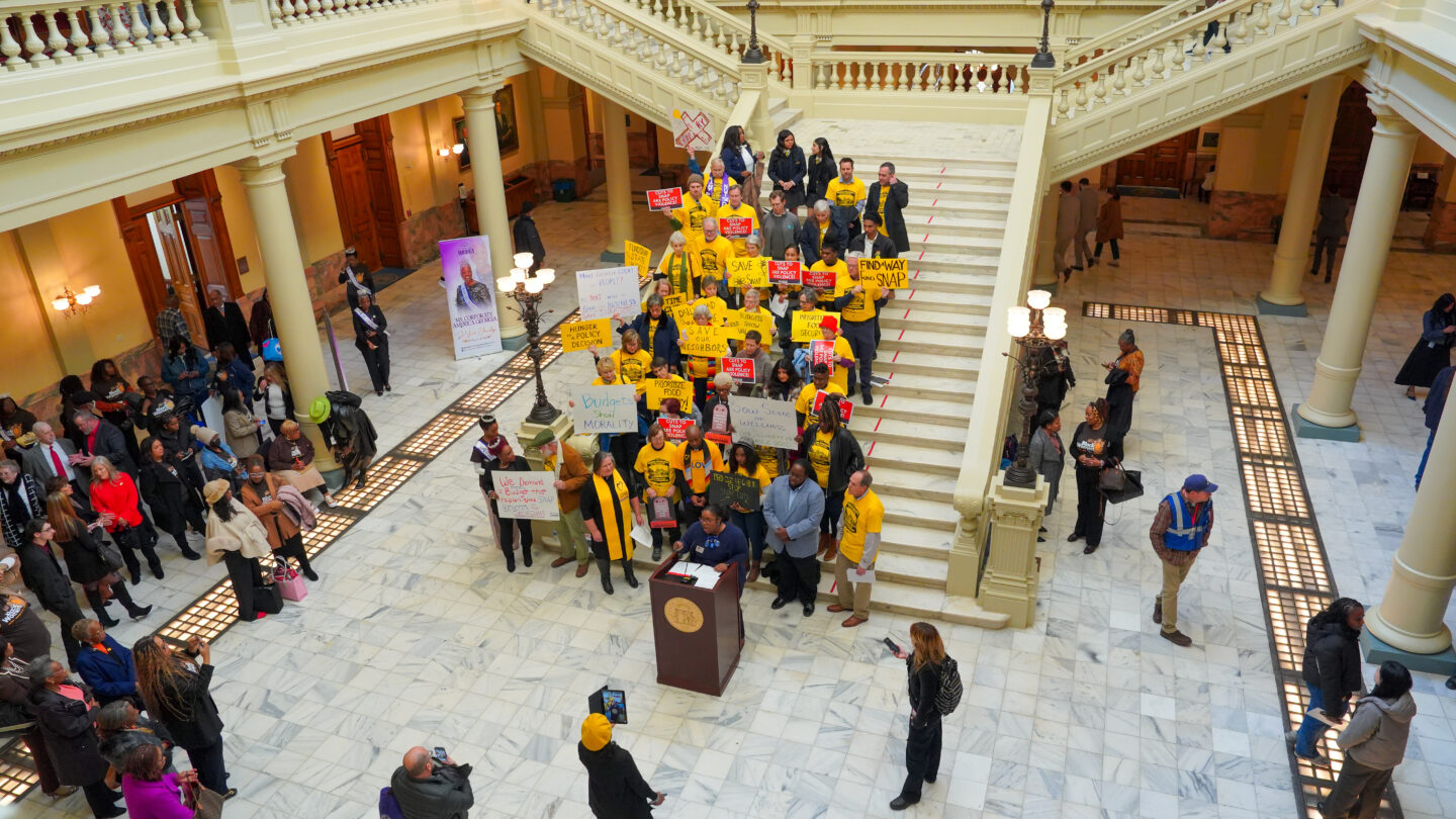 A group of advocates wearing yellow shirts stand on the steps of the Georgia State Capitol
