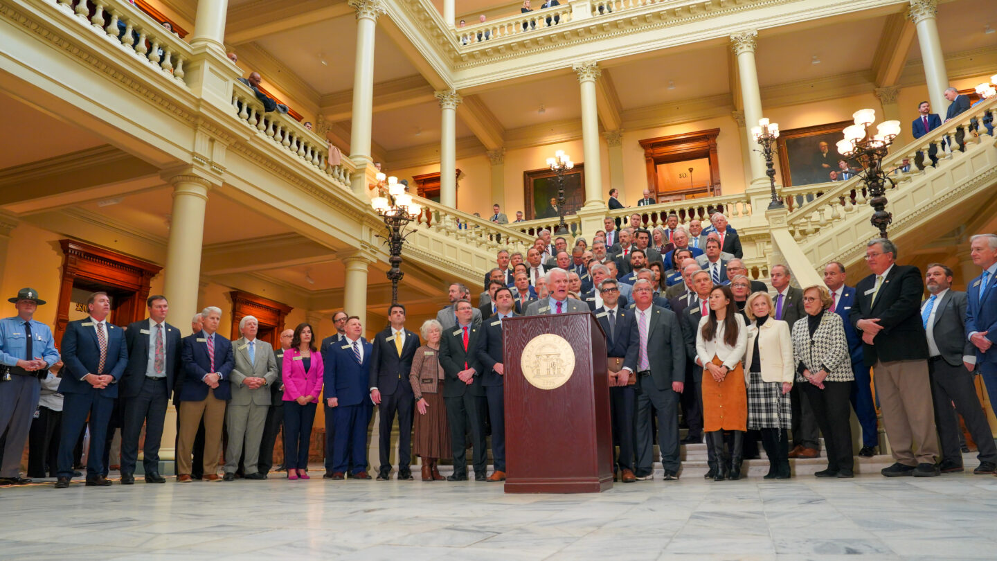 A group of people crowd around a podium at a news conference at the Georgia State Capitol.