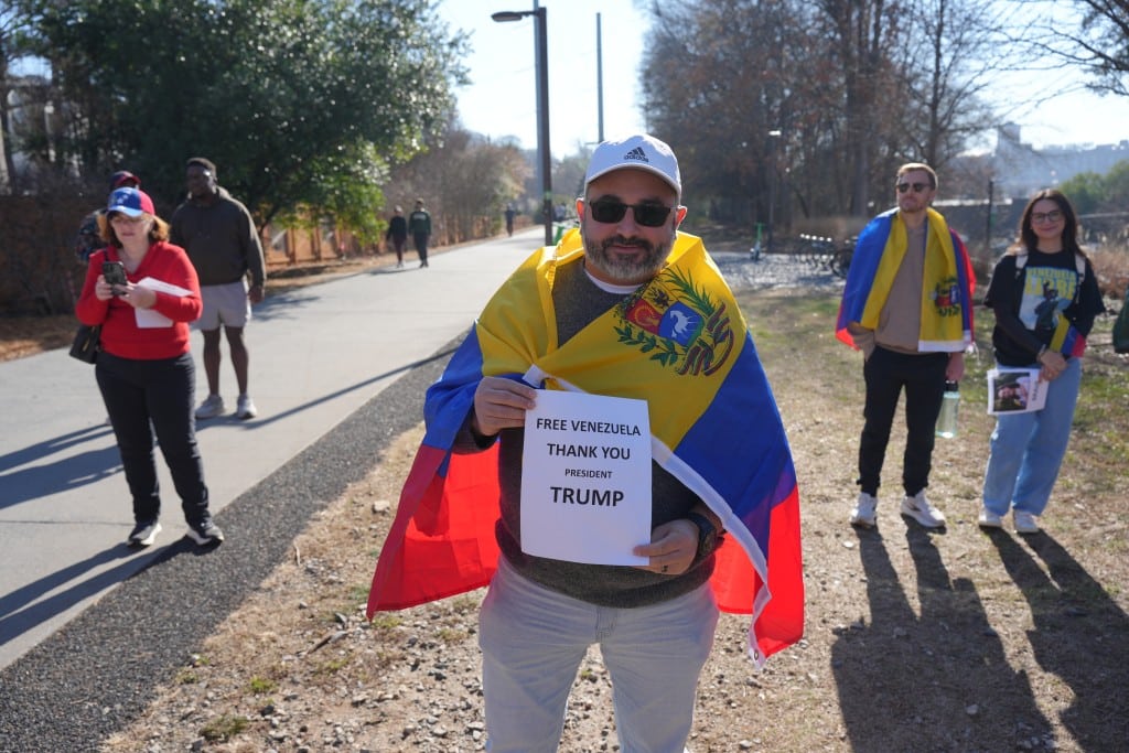 A man draped in the Venezuelan flag holds a sign praising Donald Trump.