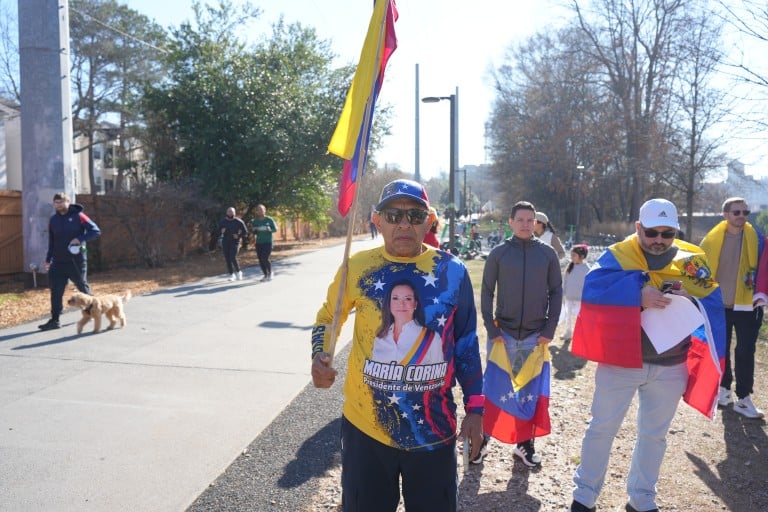 A man wearing a shirt with Maria Corina Machado's face holds a Venezuelan flag.