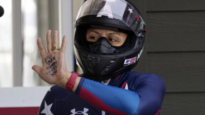 A woman in a bobsledding outfit waves