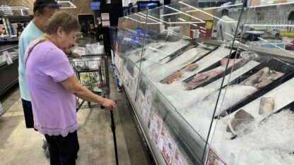 Two people look at the prices of fish at a grocery store