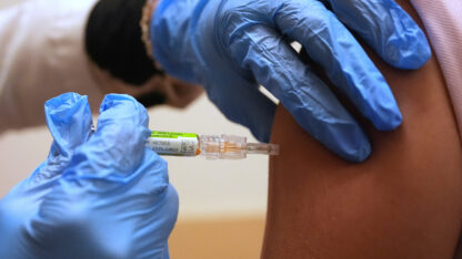 A professional in blue latex gloves administers a vaccine shot.