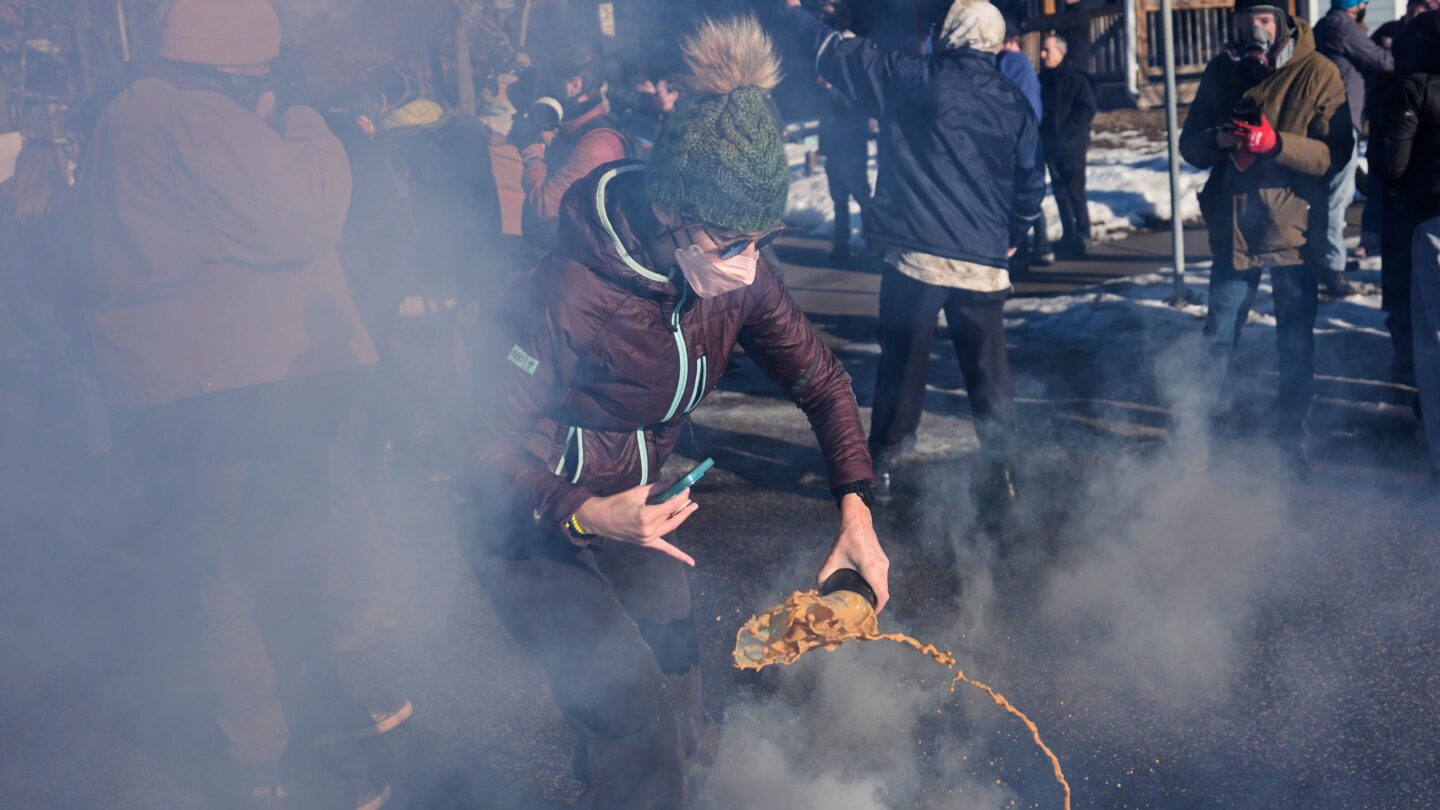 A person pours liquid on a tear gas canister in the street among a crowd of people