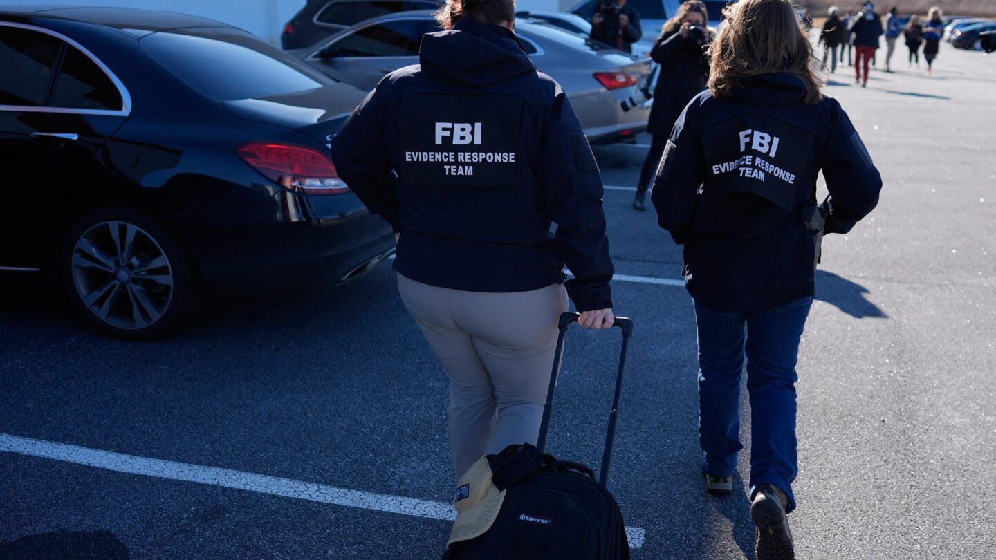 FBI officers walk through a parking lot outside of a building