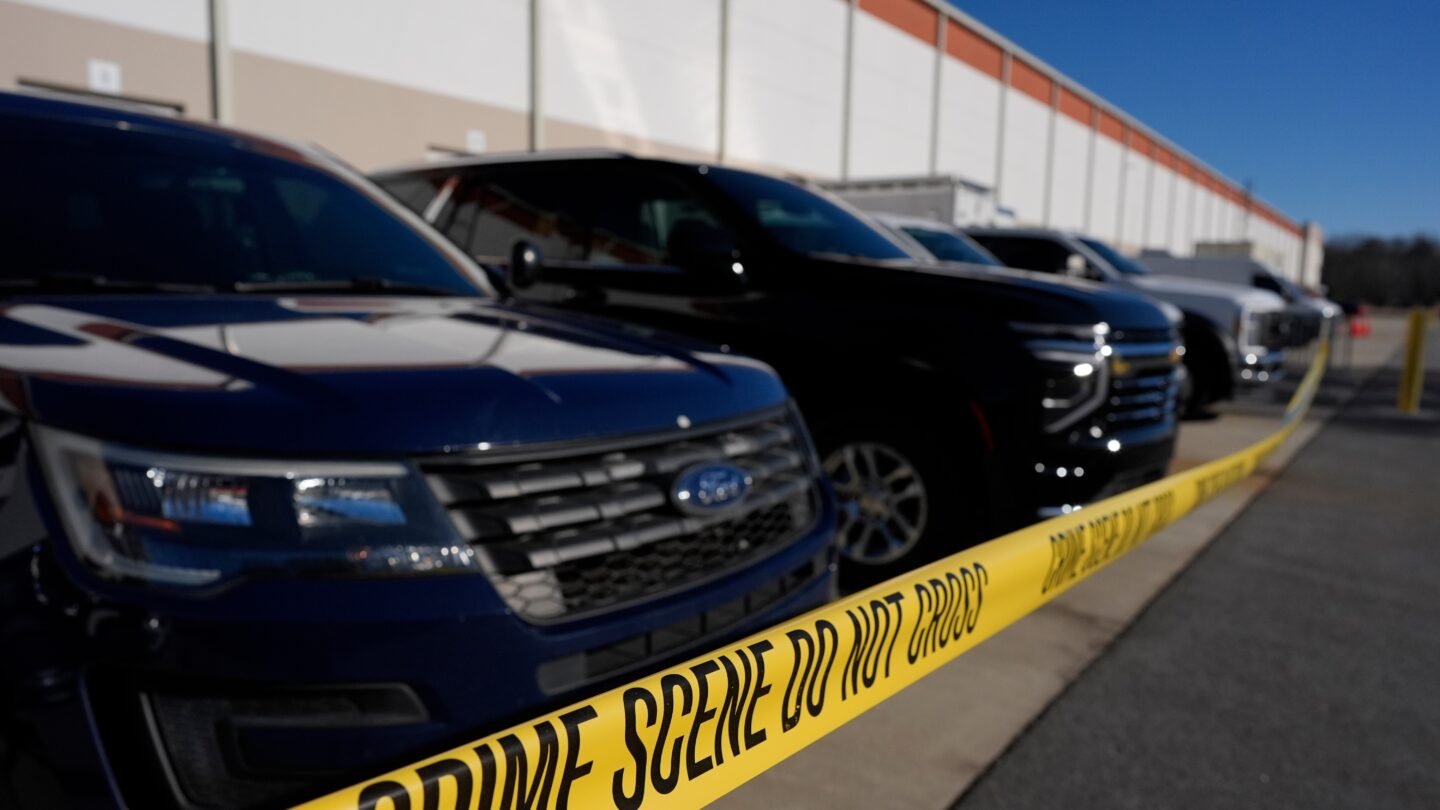 A row of vehicles sit parked behind crime scene tape outside of a building