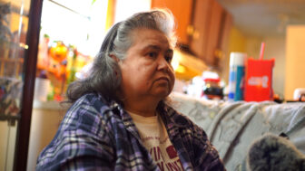 A woman sits inside a home, looking to the right