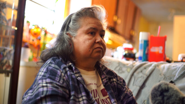 A woman sits inside a home, looking to the right