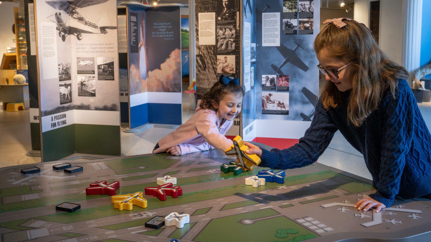 Children playing with wooden planes on runway activity table.