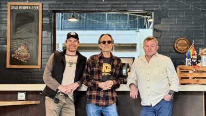Three men stand under a sign for WILD HEAVEN BEER.