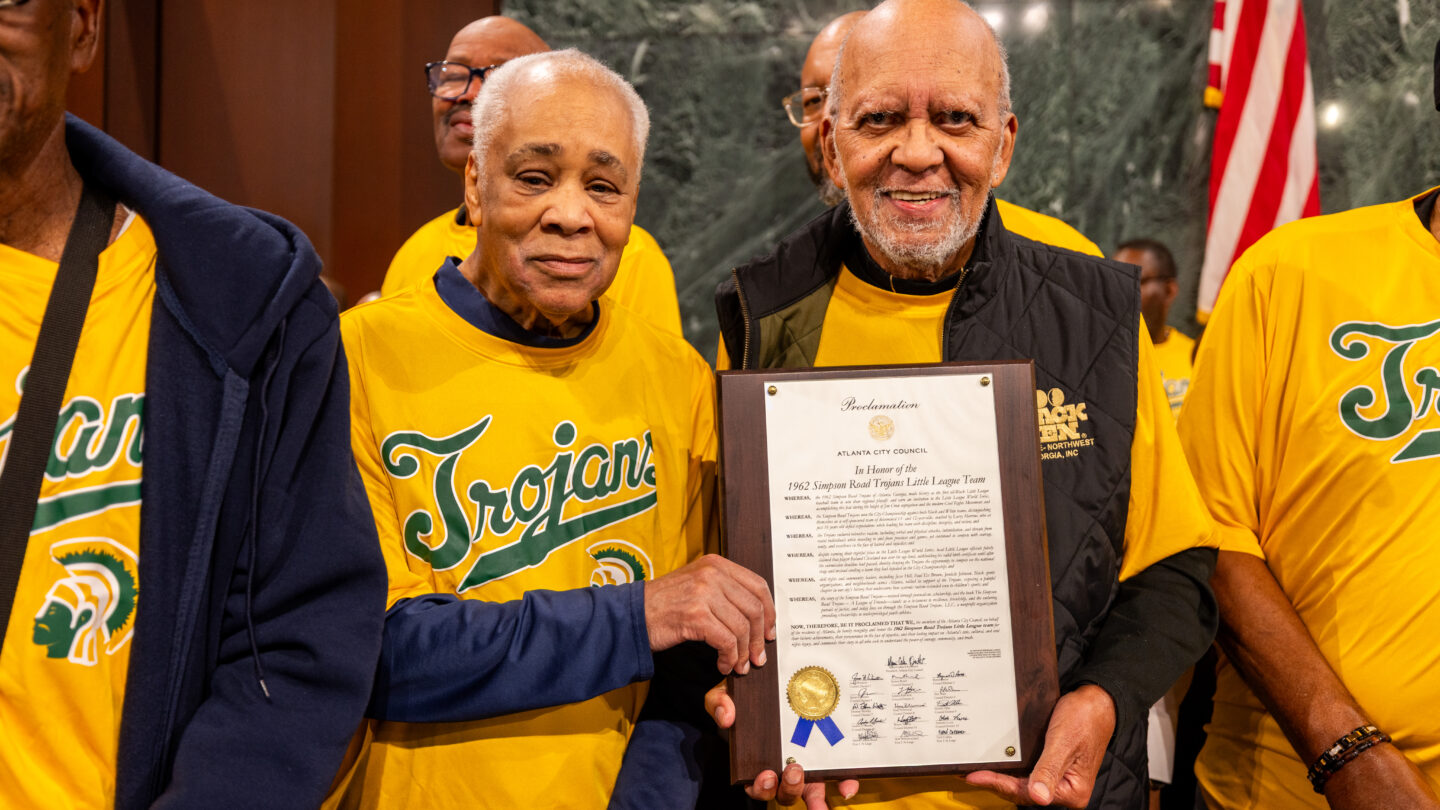 A group of people wearing yellow Trojans jerseys hold up a plaque