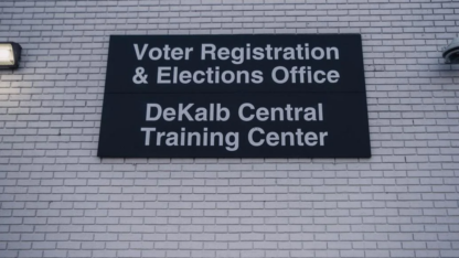 A black sign on a white brick wall that indicates the Voter Registration and Elections Office