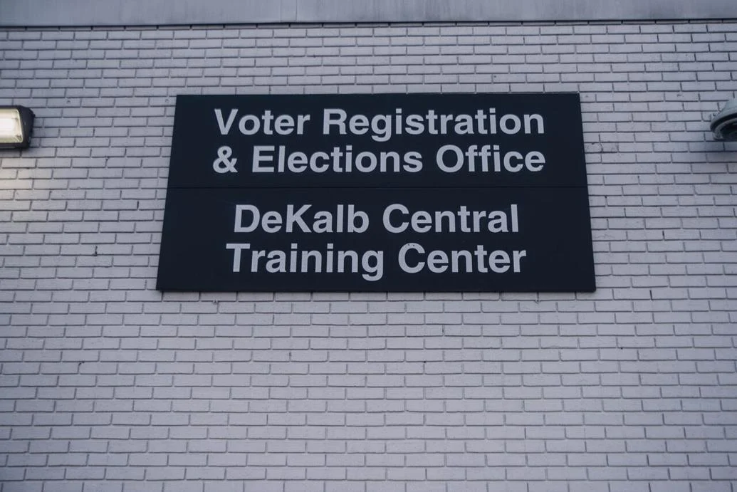 A black sign on a white brick wall that indicates the Voter Registration and Elections Office