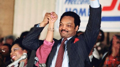 Jesse jackson holds his wife's hand in celebration in front of a cheering crowd