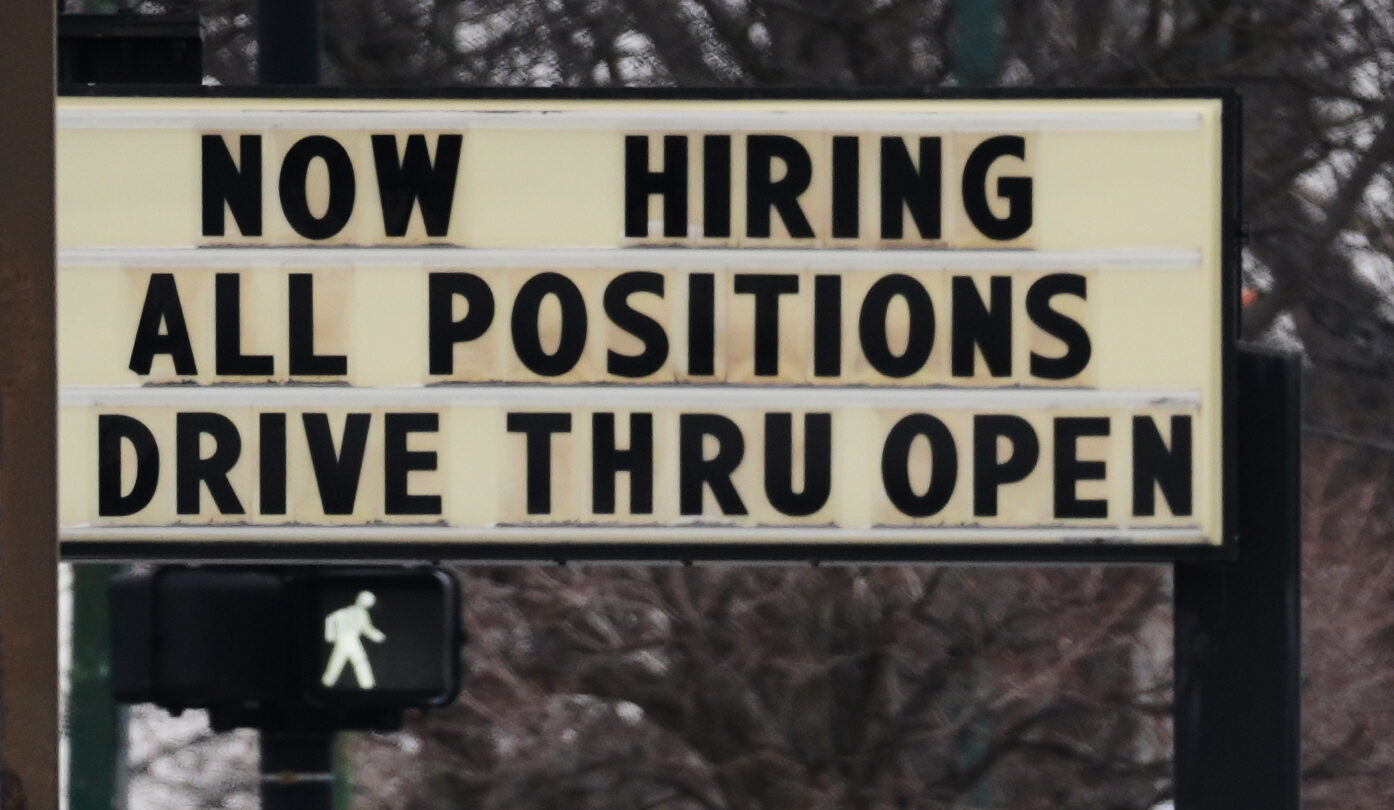 A sign with black letters on a white background says that a business is hiring