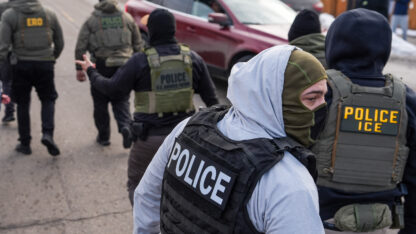 Federal agents wearing vests that say Police ICE walk on a sidewalk