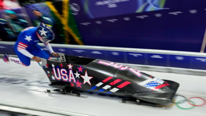 A woman runs behind a bobsled pushing it along the ice in the winter olympics