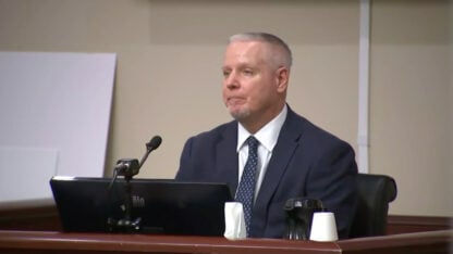 Colin Gray sits on the stand in a suit and tie.
