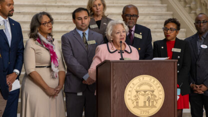 A group of georgia lawmakers in business attire stand behind a podium at the georgia state capitol