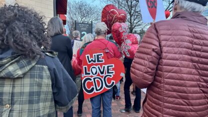 A former CDC workers marches with a red sign that says WE LOVE CDC.