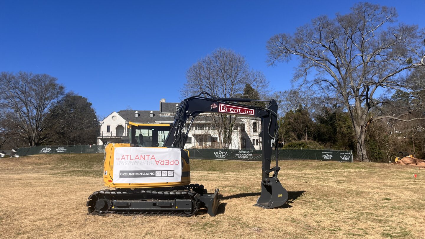 Yellow excavator with “Molly Blank Center for Opera and the Arts” groundbreaking banner in front of the Bobby Jones Clubhouse.