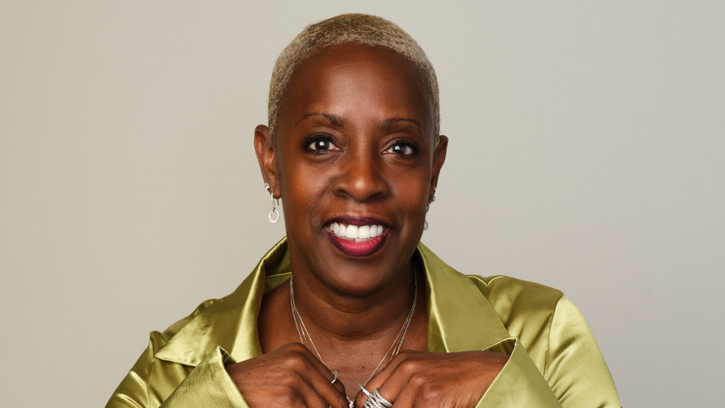 Nasha Thomas smiles in a studio portrait, wearing a green jacket against a neutral background.
