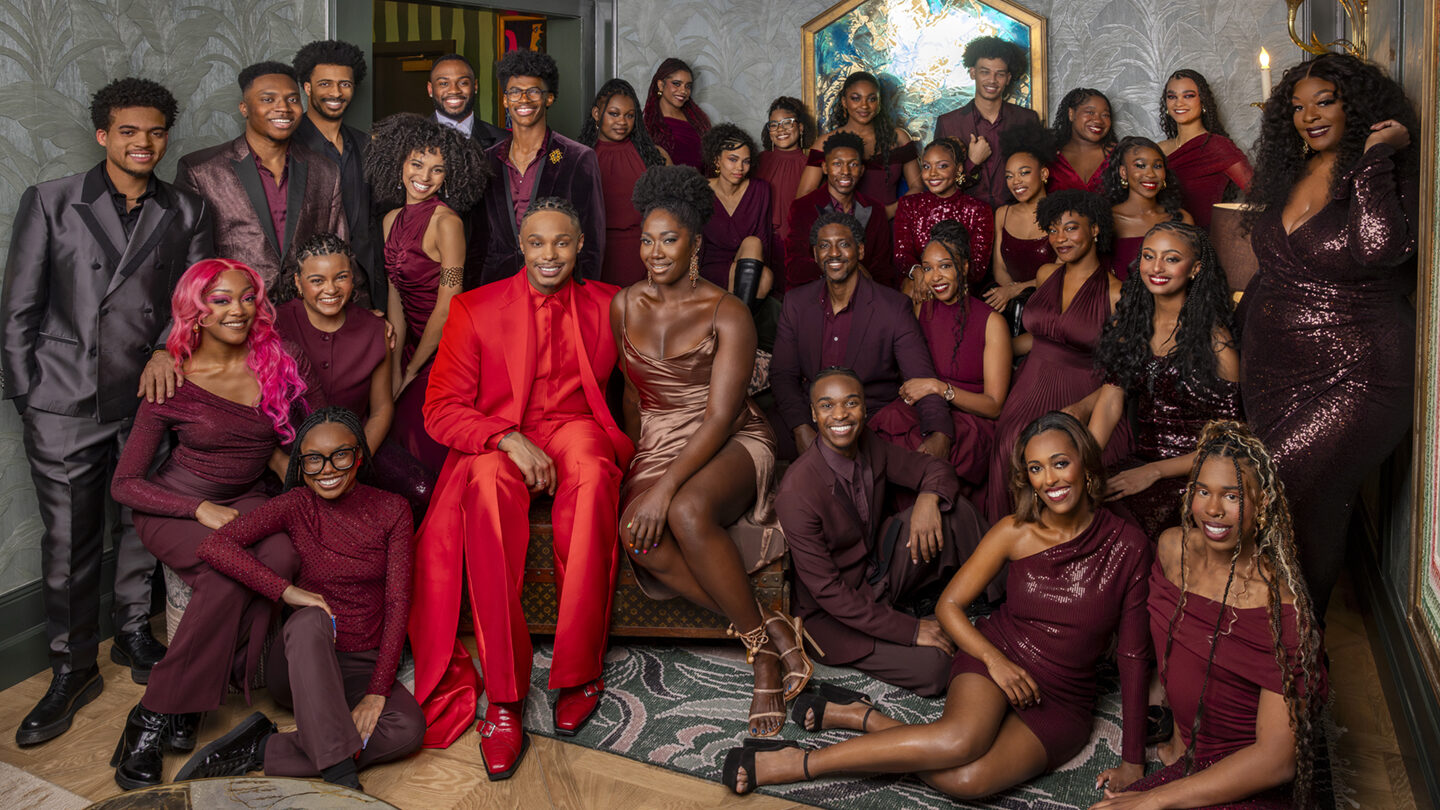 Large group in coordinated burgundy and red formalwear poses in a lounge before SCAD’s BAM concert.