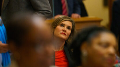 A state lawmaker looks upward during a debate surrounded by other lawmakers