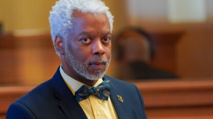 state representative dexter sharper stands in a suit with a yellow shirt and bow tie